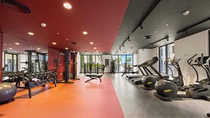 Un gimnasio con equipo de ejercicio, espejos y suelo rojo.