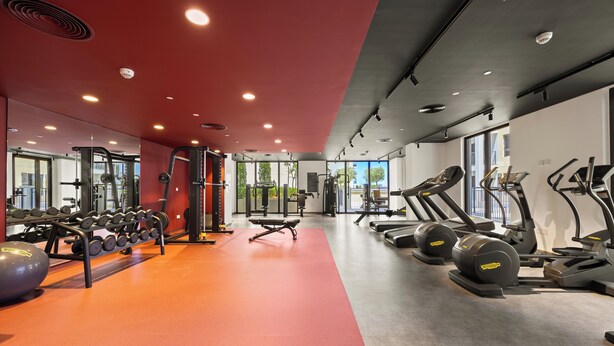 Una palestra con attrezzature per esercizi, specchi e pavimento rosso.