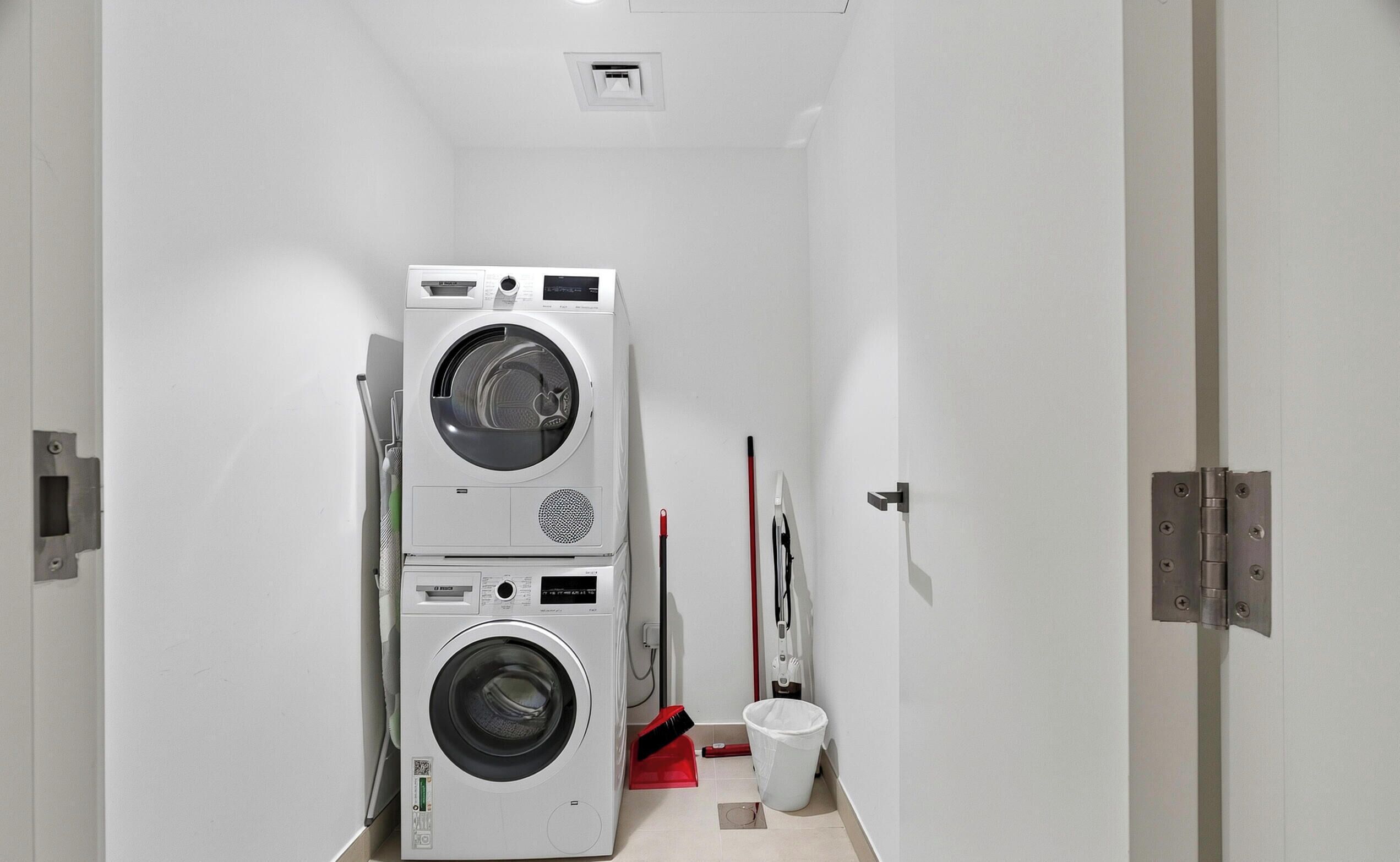 A laundry room with stacked washing machines and a mop.