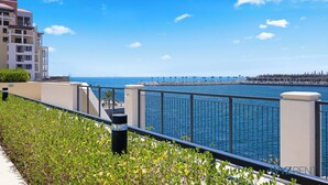 Vista sulla costa con balcone che si affaccia sul mare, una passeggiata e una città all'orizzonte.