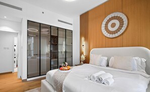 Habitación de hotel moderna con una cama grande, un panel decorativo de madera, un armario de vidrio y vista al área de lavandería.