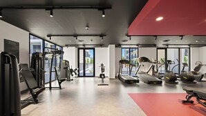 Una palestra moderna con diverse attrezzature per l'esercizio fisico, ampie finestre e una parete di accento rosso.