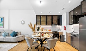 A modern kitchen with a dining area, a sofa, and a painting on the wall. - WYZ RENT|Bayfront 1BR in La Sirene 2 Seaport View (Dubai)