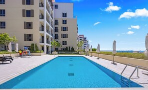 Una piscina con una profundidad de 1,2 metros, rodeada por un edificio con balcones y mobiliario exterior.