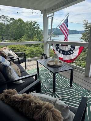 A covered outdoor seating area with a view of a body of water, a flag, and a table with a candle and a vase.
