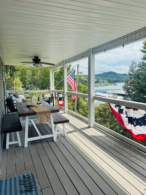 A covered outdoor deck with a table and benches, overlooking a lake and hills.
