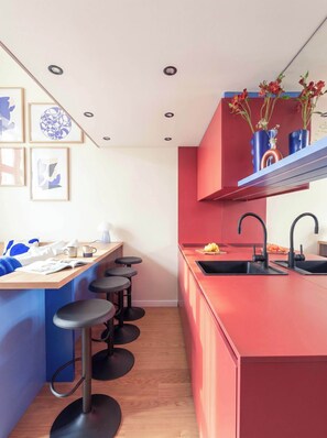Une cuisine moderne avec un îlot central rouge, des tabourets de bar et un évier doté de robinets noirs.