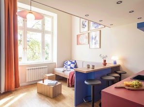 A modern kitchen with a bar area, a dining table, and a window with curtains. - TurnKey | Vinohrady Modern Loft Apartment II (Prague 3)
