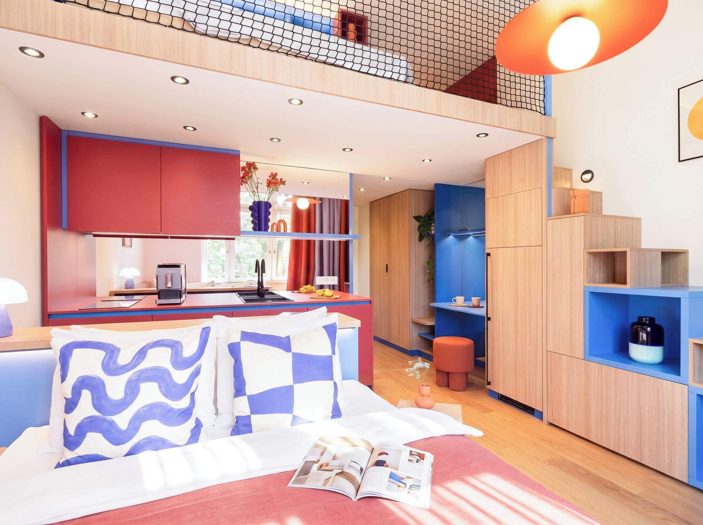 Ein modernes, kompaktes Wohnzimmer mit Küchenzeile, Essbereich und Schlafzimmer, inklusive Bett und Lesematerialien.