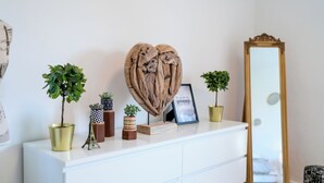 A white dresser with decorative items including a heart-shaped sculpture, framed picture, and potted plants.