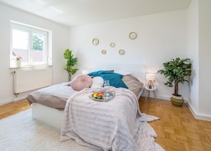 Ein Schlafzimmer mit Bett, Nachttischen, einem Fenster und einer Topfpflanze.