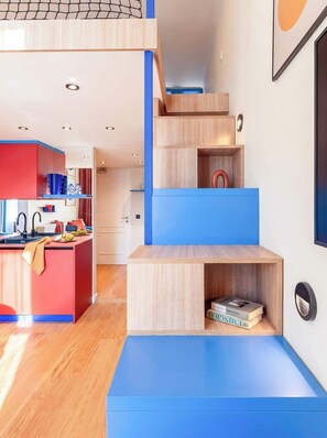 A modern kitchen with a red island, a blue staircase, and a wooden bookshelf. - TurnKey | Vinohrady Modern 2BR Ap. with Balcony (Prague 3)