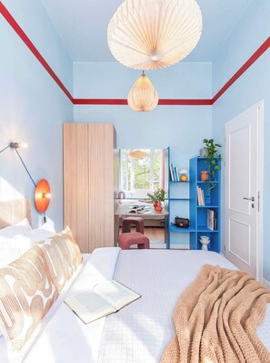 A bedroom with a bed, bedside table, lamp, wardrobe, desk, chair, and a blue shelving unit with books and plants. - TurnKey | Vinohrady Modern 2BR Ap. with Balcony (Prague 3)