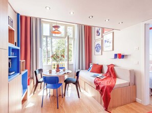 A modern living room with a sofa, chairs, a dining table, and a large window with curtains.