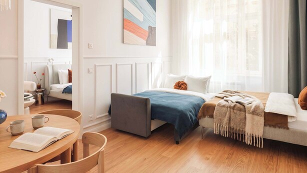 Ein modernes, helles Schlafzimmer mit Bett, Nachttisch und einer Leseecke mit Sessel und Tisch.