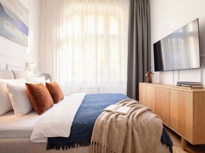 A hotel room with a bed, a TV, a wooden cabinet, and a window with sheer curtains.