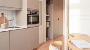 Eine moderne Küche mit integrierten Geräten, ein Essbereich mit einem Holztisch und Stühlen sowie Blick in einen Wohnraum.