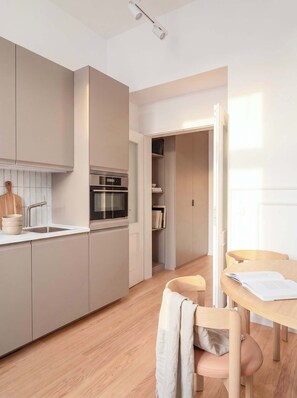 Eine moderne Küche mit integrierten Geräten, ein Essbereich mit einem Holztisch und Stühlen sowie Blick in einen Wohnraum.
