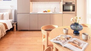Eine moderne Küche mit integrierten Geräten, ein Essbereich mit Holztisch und Stühlen sowie ein Bett mit weißem Kopfteil.