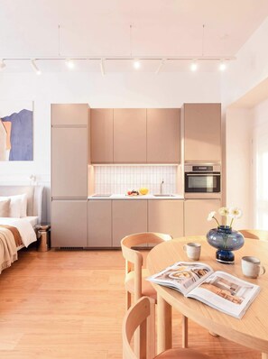Eine moderne Küche mit integrierten Geräten, ein Essbereich mit Holztisch und Stühlen sowie ein Bett mit weißem Kopfteil.
