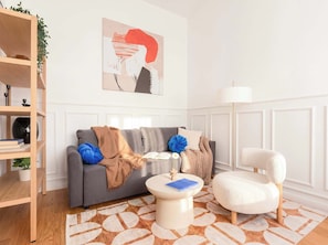 Ein modernes Wohnzimmer mit einem grauen Sofa, einem weißen Sessel, einem runden Couchtisch und einem Bücherregal.