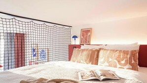 Une chambre d’hôtel avec un lit, une fenêtre protégée par un moustiquaire, une lampe et un tableau encadré au mur.