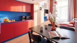 Une cuisine moderne avec des meubles de rangement rouges et bleus, une table à manger avec des chaises, une machine à café et un vase rempli de fleurs.