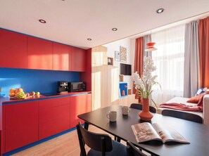 A modern kitchen with red and blue cabinets, a dining table with chairs, a coffee machine, and a vase with flowers.
