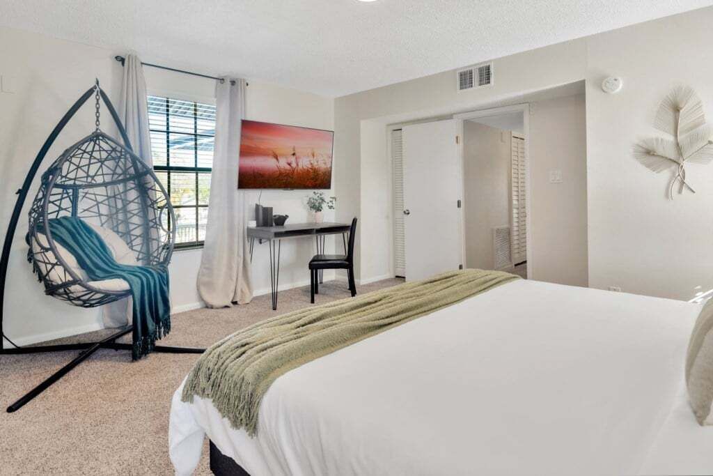 A bedroom with a bed, a desk, a chair, and a hanging chair.
