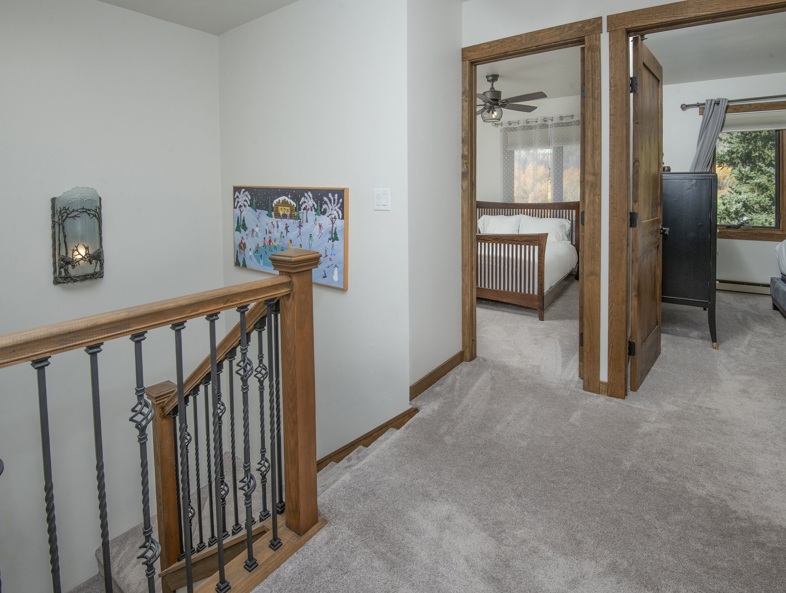 A hallway with a wooden railing, a painting, a ceiling fan, and a bed in the background.