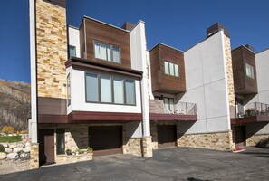Ein modernes Wohngebäude mit Fassade aus Stein und Holz, mehreren Garagentoren und freiem Blick auf die umliegende Landschaft.