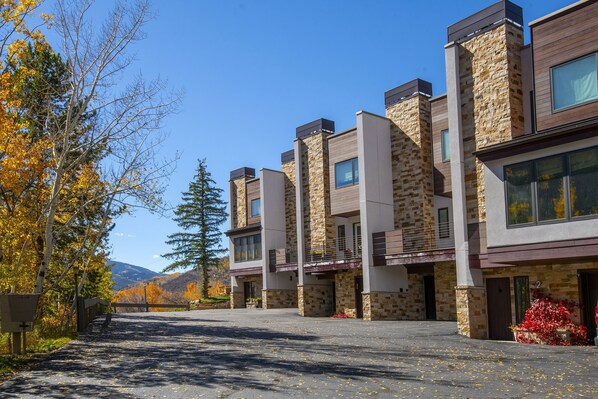Ein modernes, mehrgeschossiges Gebäude mit Fassade aus Stein und Holz, großen Fenstern und einer gepflasterten Auffahrt.