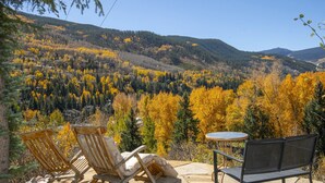 Eine Terrasse mit zwei Holzstühlen und einem kleinen Tisch, mit Blick auf ein bewaldetes Tal im Herbstlaub.