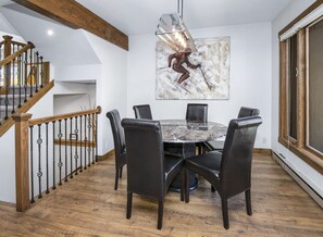 Ein Essbereich mit einem runden Tisch, sechs Stühlen, einer Chandelüster und einer Treppe mit Holzwertungen.