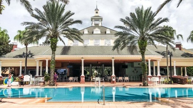 A hotel with a swimming pool, palm trees, and outdoor seating. - Sunset Games Retreat At Reunion Resort 6 Bedroom Villa (Kissimmee)