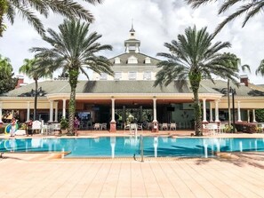 A hotel with a swimming pool, palm trees, and outdoor seating. - Sunset Games Retreat At Reunion Resort 6 Bedroom Villa (Kissimmee)
