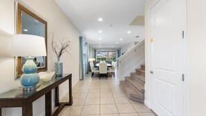 A hallway with a dining area at the end, featuring a staircase and a white door. - Sunset Games Retreat At Reunion Resort 6 Bedroom Villa (Kissimmee)