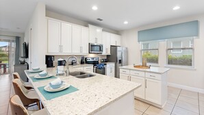 A modern kitchen with white cabinets, stainless steel appliances, and a large island with seating. - Sunset Games Retreat At Reunion Resort 6 Bedroom Villa (Kissimmee)