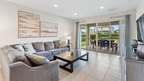 A modern living room with a grey sofa, a glass coffee table, and two abstract paintings on the wall. - Sunset Games Retreat At Reunion Resort 6 Bedroom Villa (Kissimmee)