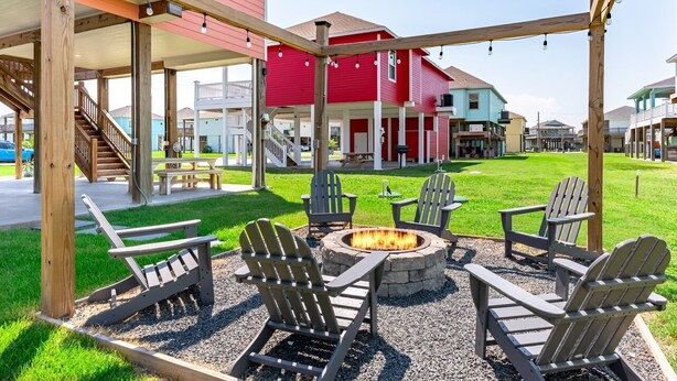 An outdoor patio area with Adirondack chairs, a fire pit, and a wooden pergola. - Sea Glass Retreat 3 Bedroom Home (Port Bolivar)