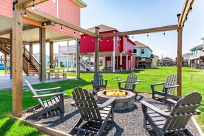 Uma área de varanda externa com cadeiras Adirondack, lareira e pérgola de madeira.