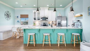 A kitchen with white cabinets, a large island with bar stools, and pendant lighting. - Sea Glass Retreat 3 Bedroom Home (Port Bolivar)