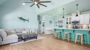 A spacious living room with a light blue wall, a ceiling fan, and a large fish decoration. - Sea Glass Retreat 3 Bedroom Home (Port Bolivar)