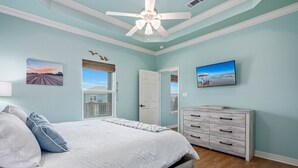 A bedroom with a bed, a dresser, a ceiling fan, and a TV. - Sea Glass Retreat 3 Bedroom Home (Port Bolivar)
