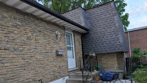 A brick house with a grey roof, a white door, and a small outdoor seating area with a table and chairs. - Cozy Private Room, Very close to Hospital, College & University, Free Parking. (Peterborough)