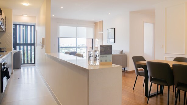 A modern kitchen with a central island, a dining area with chairs, and a large window offering a city view. - w Inviting 2BR w Balcony in Miraflores (Lima)