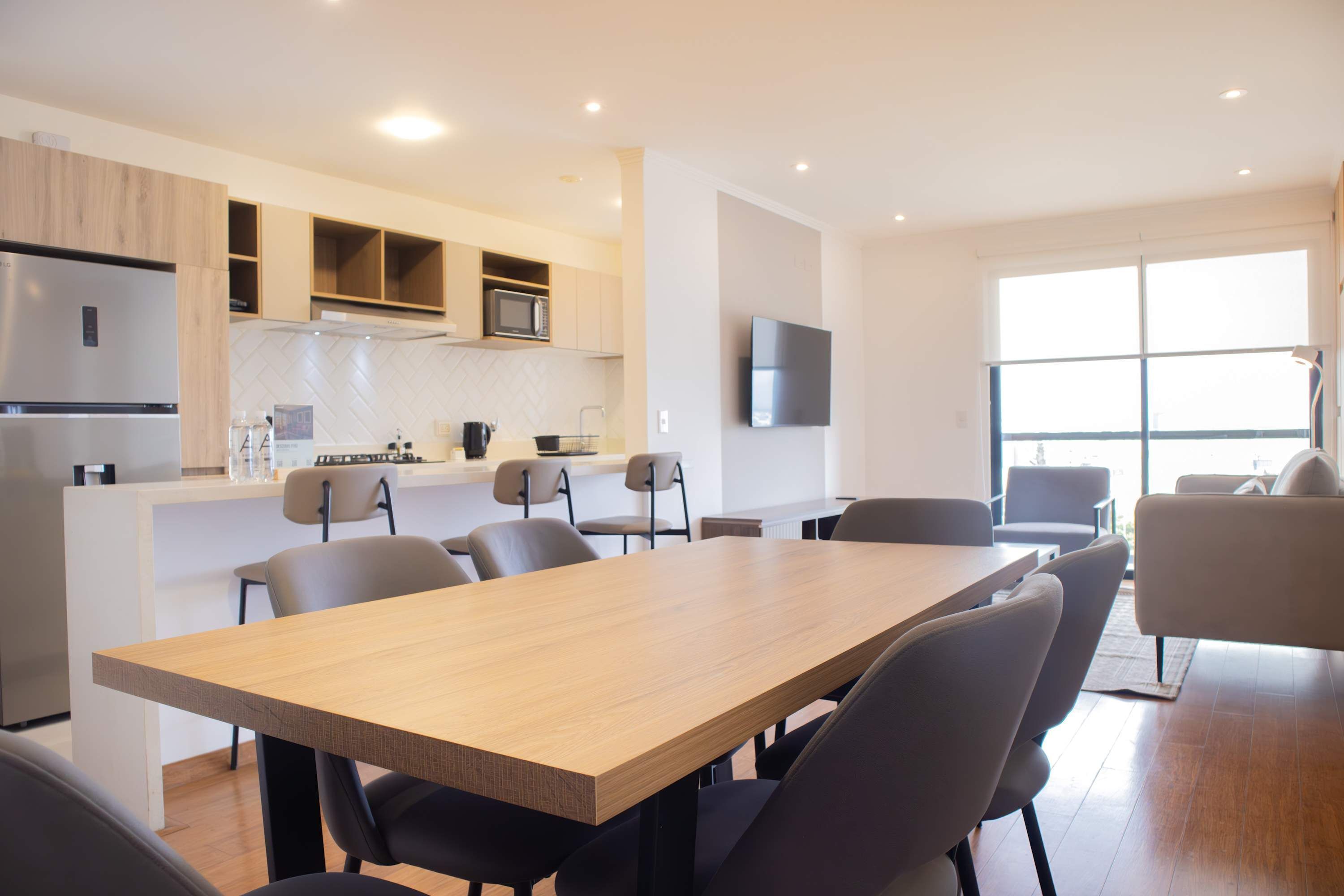 Une cuisine moderne dotée d’appareils électroménagers intégrés, un coin repas avec une grande table et des chaises, et un téléviseur fixé au mur.