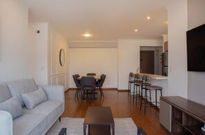 A modern living room with a sofa, dining table, chairs, and a kitchen area with bar stools. - w Inviting 2BR w Balcony in Miraflores (Lima)