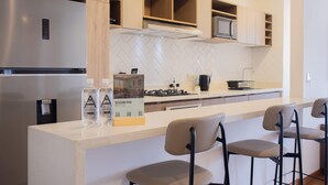 A modern kitchen with a stainless steel refrigerator, a microwave, a gas stove, and a tiled backsplash. There are two bar stools and a water dispenser. - w Inviting 2BR w Balcony in Miraflores (Lima)