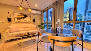 Una sala moderna con sofá, mesa de centro y mesa de comedor con sillas. Hay un ventanal con vista a la ciudad.